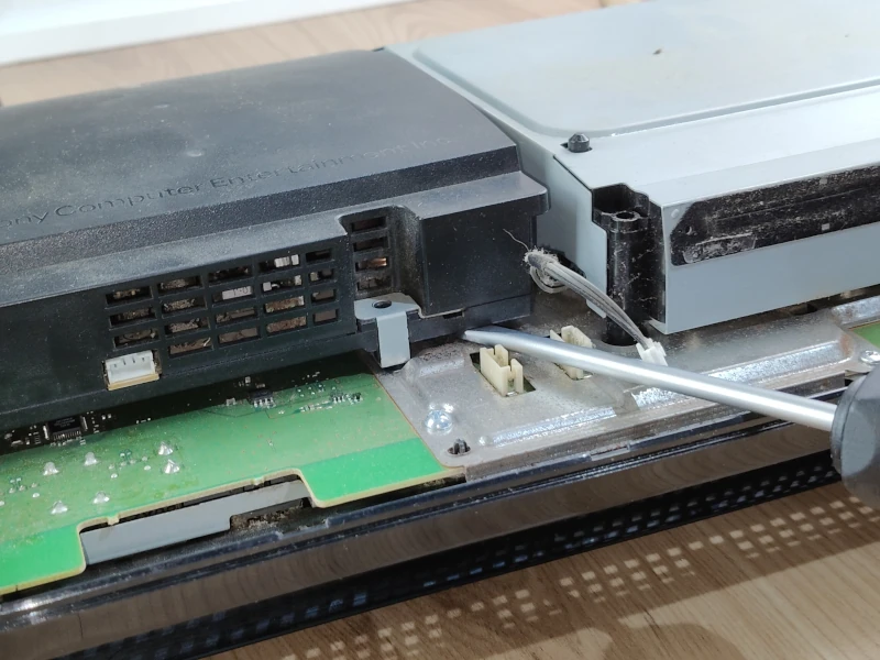 Demontaż PlayStation 3 fat - podważanie zasilacza za pomocą śrubokręta
